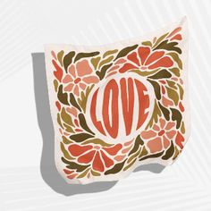 an orange and green pillow with the word love on it, surrounded by red flowers