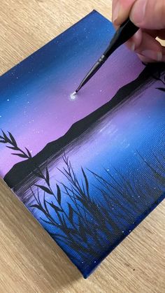 a person is using a brush to paint a landscape with blue, purple and black colors