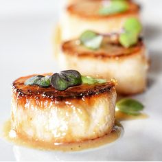 three pieces of food on a white plate with sauce and green leafy garnish