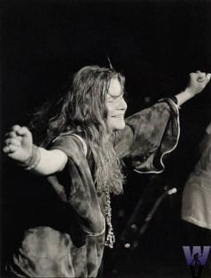 a woman with long hair and glasses is holding her arms in the air while standing on stage