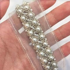 a hand is holding a bracelet with pearls and mesh on it's wrist,