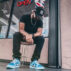 a man sitting on top of a chair in front of a barbershop wearing a hat