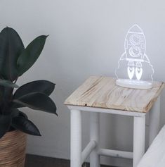 a small wooden table with a light on it next to a potted plant and bed