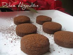 six chocolate cookies sitting on top of a white plate next to red flowers and the words duke algodon above them