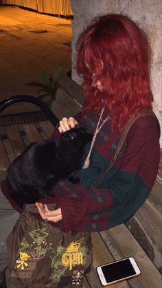 a woman with red hair sitting on a bench holding a black cat in her lap