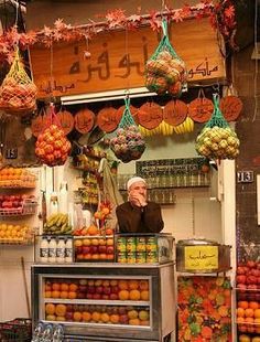 an outdoor market with lots of fruits and vegetables hanging from it's ceiling,