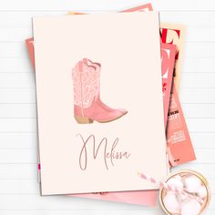 a pink cowboy boot is on top of some magazines and a glass of ice cream