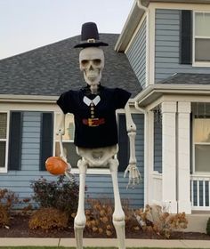 a skeleton with a top hat holding an orange ball in front of a house