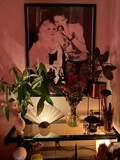 a table topped with vases and plants next to a wall mounted photo on the wall