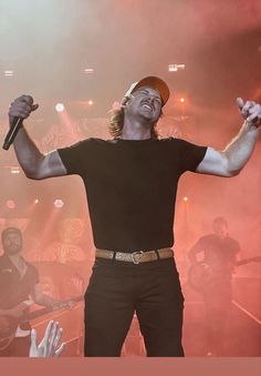 a man with his arms up in the air while singing into a microphone on stage