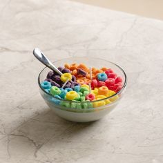 a glass bowl filled with cereal on top of a marble counter next to a spoon