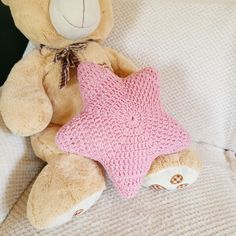 a brown teddy bear sitting on top of a bed next to a pink star pillow