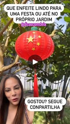 a woman standing next to a tree with two red lanterns hanging from it's branches