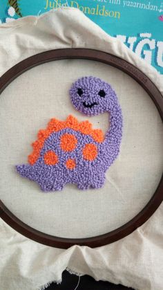 a purple and orange crocheted dinosaur on a white background with a brown frame