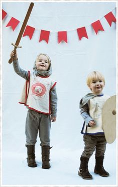 two young boys dressed in medieval clothing holding swords and shields, standing next to each other