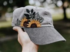 a person holding up a hat with a sunflower embroidered on the front and side