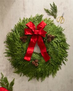 a green wreath with red ribbon and pine cones