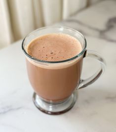 a glass mug filled with liquid sitting on top of a white marble countertop next to a window