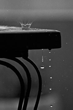 a black and white photo of a bench with water droplets on it