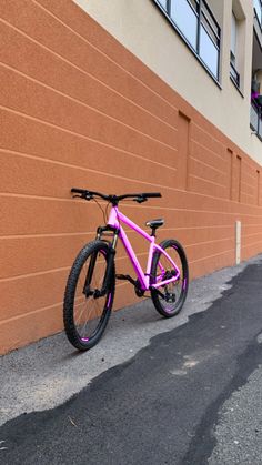 a pink bike leaning against a wall on the side of a road in front of a building