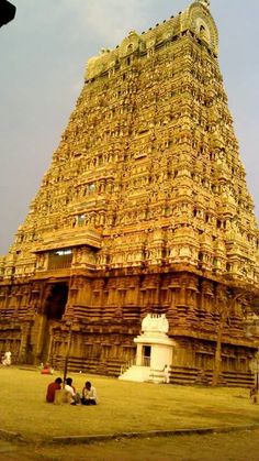 people sitting on the ground in front of a tall structure with many carvings and designs