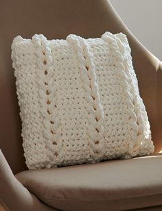 a white crocheted pillow sitting on top of a brown chair