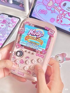 a person holding a pink cell phone in front of two other phones with hello kitty stickers on them