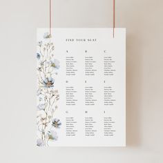 a seating chart with blue flowers hanging from the side on a white wall next to a pair of scissors