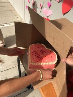 a heart shaped cake in a cardboard box being handed by someone's hand over it