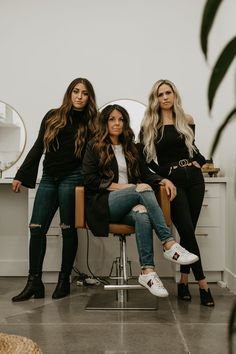 three women sitting on a chair in front of a mirror