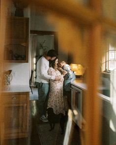 a man and woman standing in a kitchen next to each other holding a small child