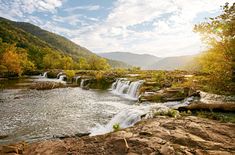 there is a small waterfall in the middle of this river with rocks and trees around it