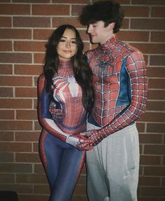 a man and woman dressed as spiderman standing in front of a brick wall with their arms around each other