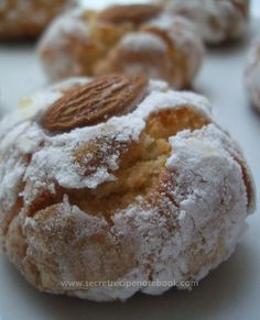 powdered sugar covered donuts with almonds on top are sitting on a white plate