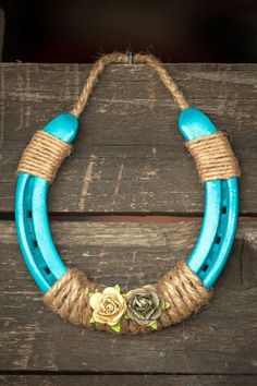 a blue and rope necklace with flowers hanging from it's sides on a wooden surface