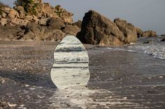 a white surfboard sticking out of the water on a beach with rocks in the background