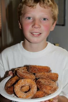 a young boy holding a plate full of doughnuts