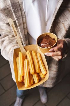 a person holding a bowl with churros in it and dipping sauce on the side