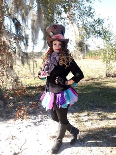 a woman wearing a hat and dress is posing for the camera with her hands on her hips