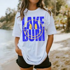 Hey there, Lake Bum! Are you ready to soak up the sun and embrace the laid-back vibes of lakeside living? Introducing our "Lake Bum" Comfort Color Tee – the perfect blend of relaxation and waterfront charm! Crafted from premium Comfort Color fabric, this tee feels as soft as a gentle breeze off the water. The playful "Lake Bum" graphic celebrates your love for lazy days by the lake, whether you're fishing off the dock or lounging in a hammock by the shore. Whether you're spending the day on a pontoon boat or simply enjoying a picnic by the water's edge, our tee is your go-to choice for casual comfort. Its relaxed fit ensures you stay cool and carefree, no matter where your lakeside adventures take you. From roasting marshmallows around the campfire to paddleboarding across the glassy surfa Graphic Print Top For Beach Season, Cotton Tops For Outdoor Beach Season, Summer Tops For Beach Season Outdoor, Lakeside Living, Soak Up The Sun, By The Lake, Pontoon Boat, Lazy Days, Comfort Colors Tee