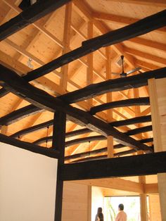 two people standing in an unfinished room with wood framing on the walls and ceiling beams