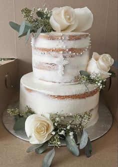 a three tiered cake with white flowers and greenery on the top is in a cardboard box