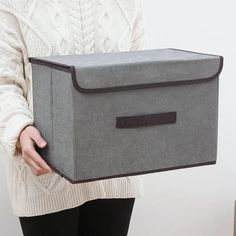 a woman is holding a gray box with black trimmings and a white sweater