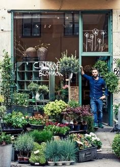 a man standing in front of a flower shop with lots of potted plants outside