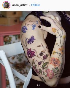 a woman with flowers painted on her arm and arms is posing in front of a chair