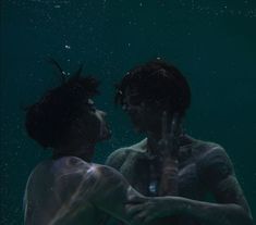 two people standing under water with their hands in the air and looking at each other