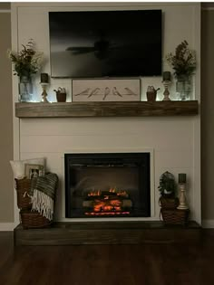 a fireplace with a flat screen tv above it and some potted plants on the mantle