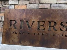 a metal sign that reads rivers lodge and hunt club on the side of a stone wall