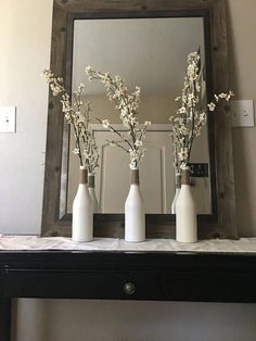 three white vases with flowers in them are sitting on a shelf near a mirror