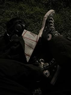 a pair of black converse shoes sitting on top of a grass covered field next to a helmet